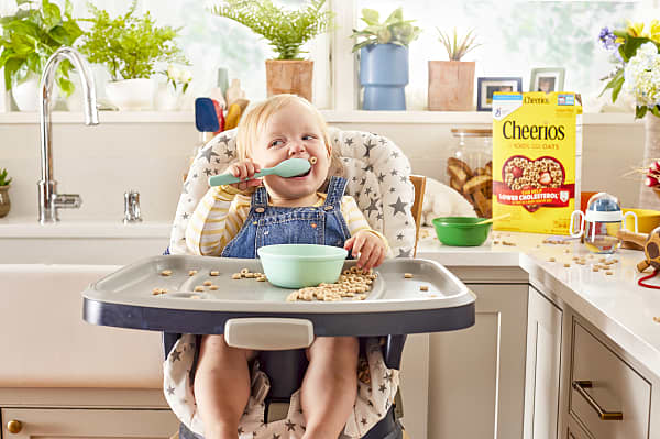 Baby sitting on a chair eating cheerios by spoon